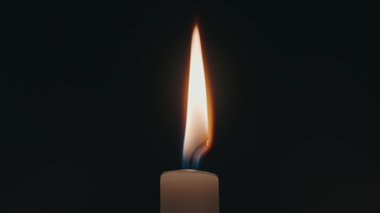Primo piano orizzontale di una singola fiamma di candela che brucia nell'oscurità.