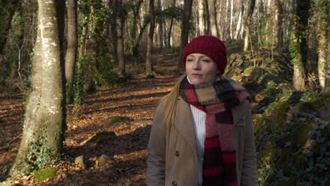 slow motion, woman in red hat and scarf walks through autumn forest, dolly out