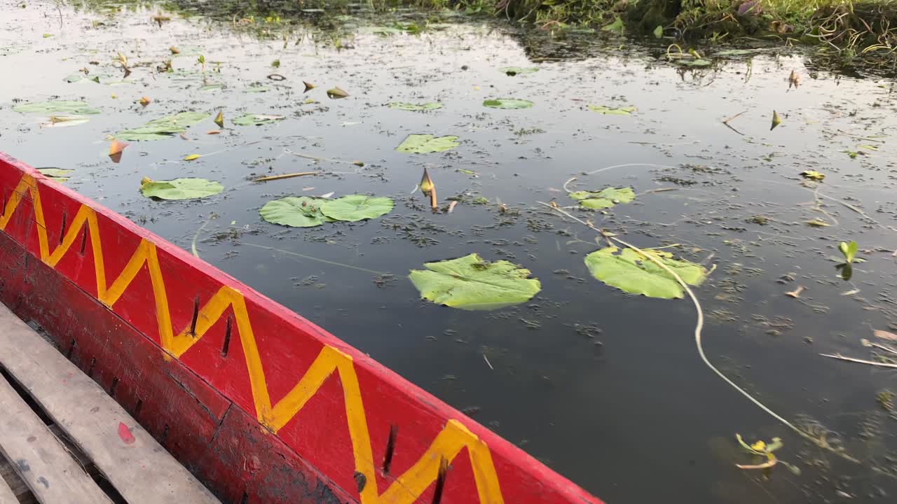 Close up of a red colored vintage boat design in traditional Indian style with water lilies and floating plants in the background.