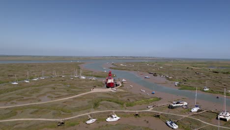 Aerial-view-towards-a-light-ship-stuck-in-mud-at-low-tide,-sunny-Tollesbury,-UK---approaching,-drone-shot