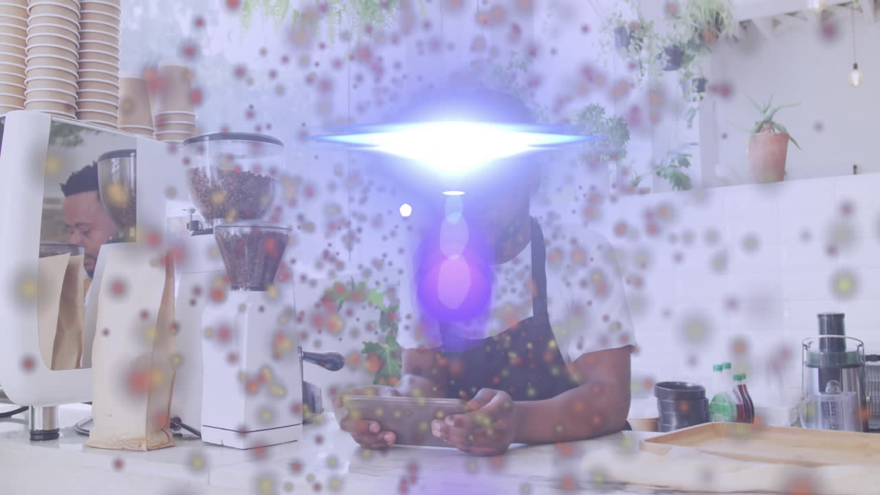 Barista using tablet behind coffee grinder in coffee shop, displaying floating dots and lens flare