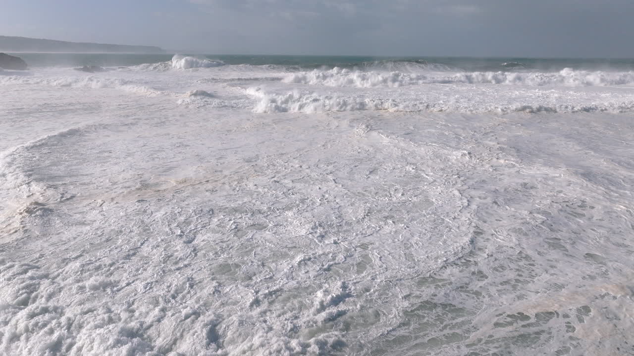 Aerial drone shot of big waves coming into shore on a day with giant waves in Nazaré, Portugal, Europe. View from beach. Big wave surfing town. Shot in ProRes 422 HQ