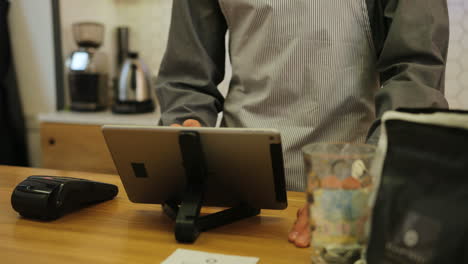 Close-up-view-of-young-woman-hands-paying-for-a-coffe-with-credit-card-while-the-male-bariste-using-a-tablet-on-the-bar-of-the-coffee-shop