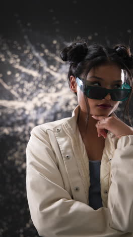 vertical video: young woman in stylish jacket holding sunglasses, expressing confidence in studio