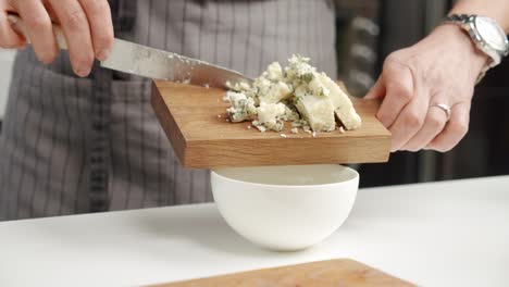 Crop-chef-adding-blue-cheese-into-bowl-from-board