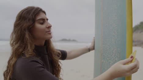 young woman waxing her surfboard on the beach