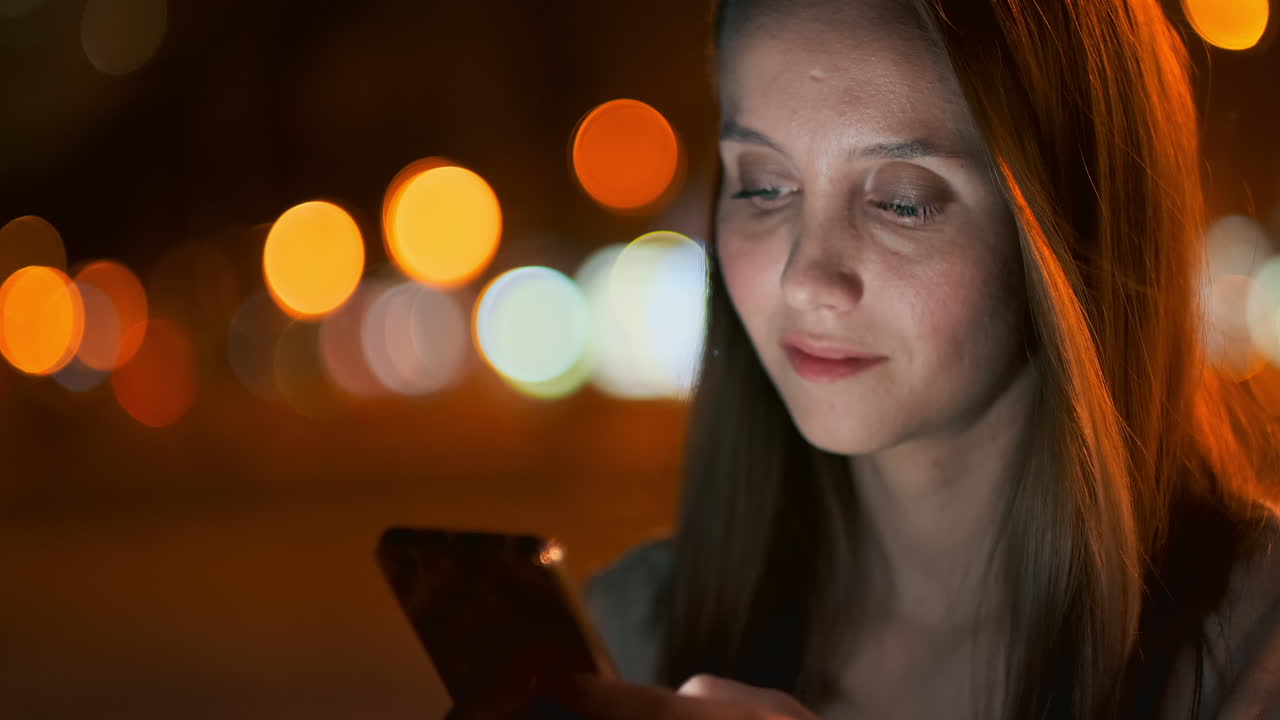 Young woman tourist travels through the night megalopolis and writes text messages on social networks about the journey holds the phone in her hands and looks at the screen of the gadget