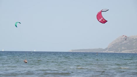 three people kiteboarding in cear blue water at mallorca balearic islands surrounded by mountain