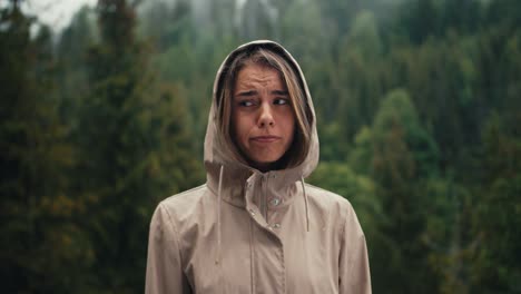 Una-Chica-Rubia-Triste-Se-Encuentra-Contra-El-Fondo-De-La-Lluvia-Forestal-En-Las-Montañas,-Está-Triste-Y-Mira-La-Cámara