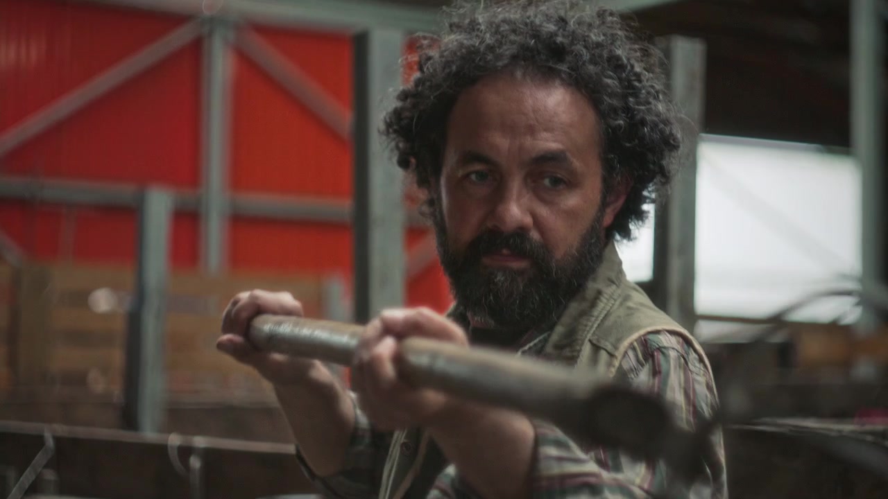 Agricoltore con la barba che mette il fieno nella stalla con un forcone