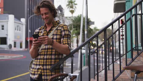 caucasian male smiling and using his phone with his bike in a street