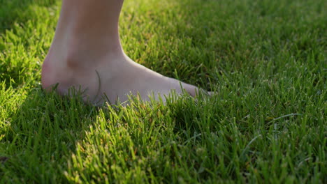 child's feet walking on green grass, close-up of walking foot