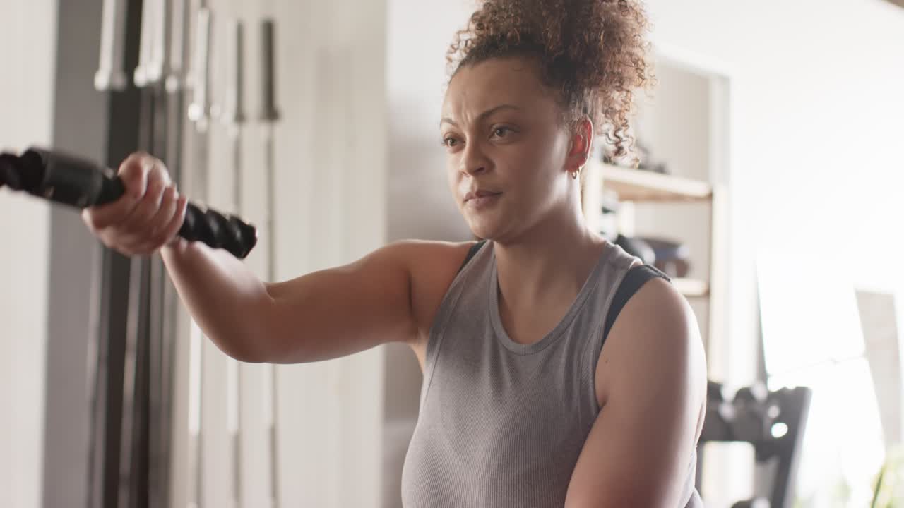 Mulher afro-americana puxando cordas de batalha onduladas alternadamente em uma academia para ganhar força