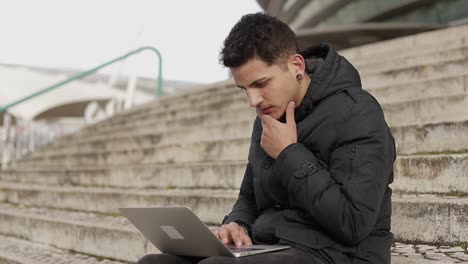 focused man working with laptop on knees outdoor