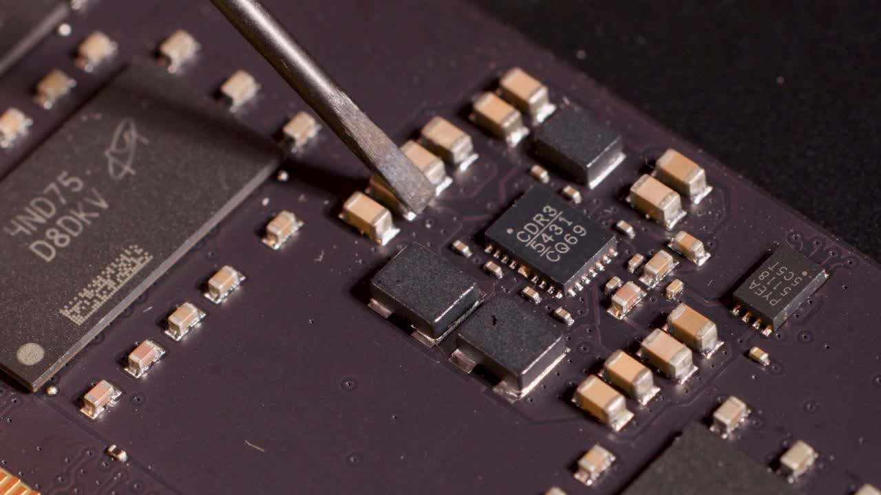 Metal tool precisely points at microchip on circuit board under bright, controlled lighting, macro view
