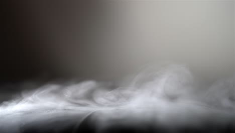 wispy strands of white fog smoke twirl move in slow motion across black leather, grey background