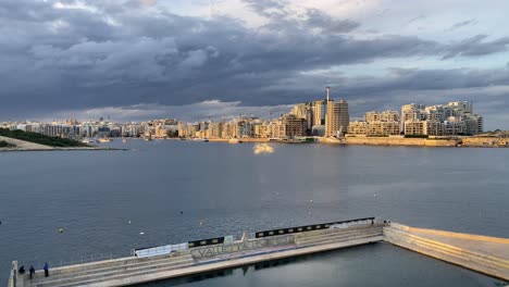 view over valleta united waterpolo pitch of sunlit sliema skyline under rain clouds