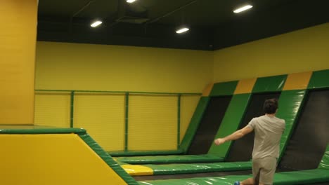 male gymnast trains on professional trampoline, springs over the barrier with the body twist and following back somersault.