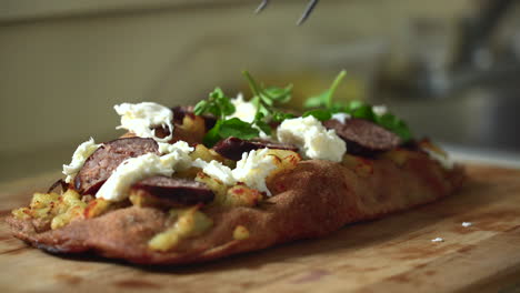 chef composing a pizza: placing leafy watercress on top of a sausage, potato and mozzarella roman style pizza