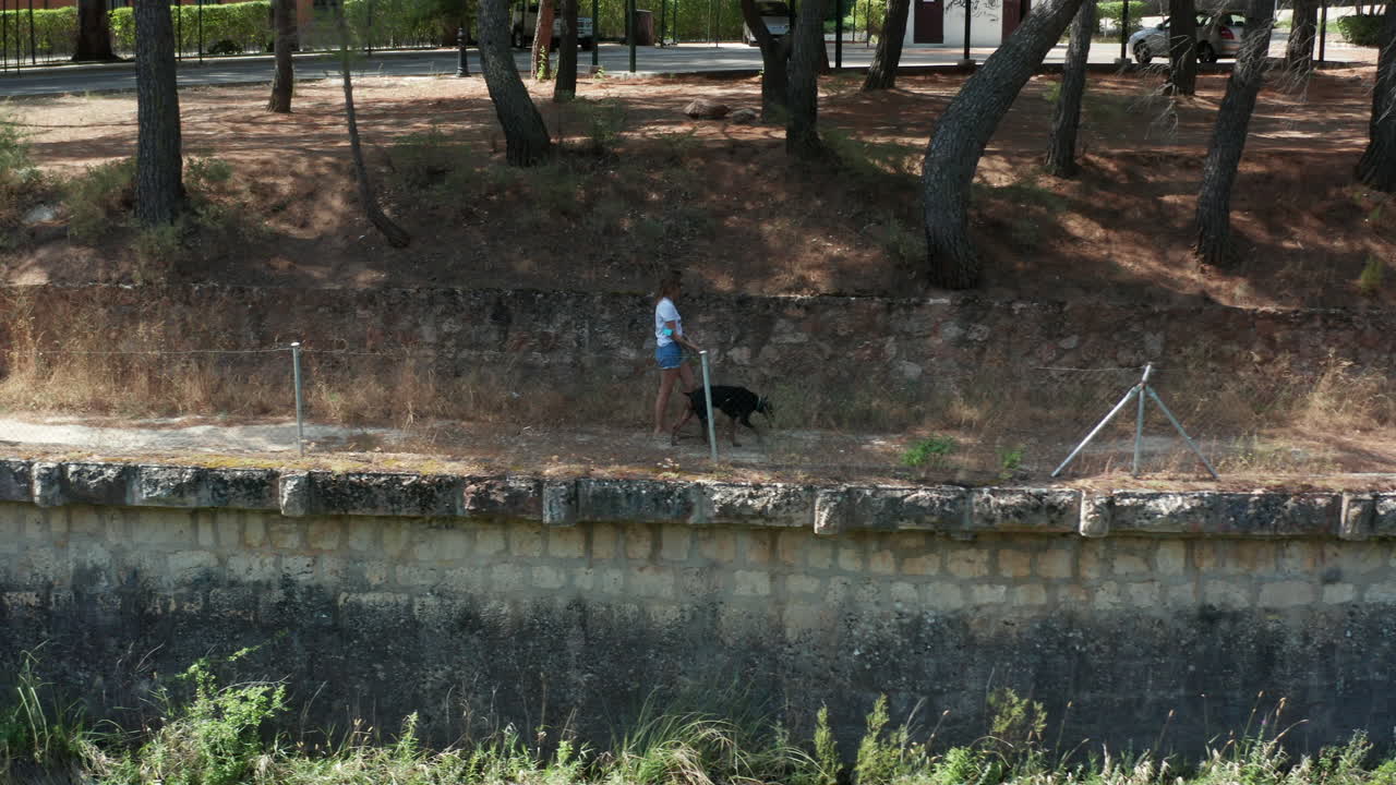 Tracking shot of young woman walking her pet dog along the footpaths of Lago de Bolarque