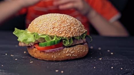 teenager hands take a tasty hamburger lying on the table close up. delicious grilled burger