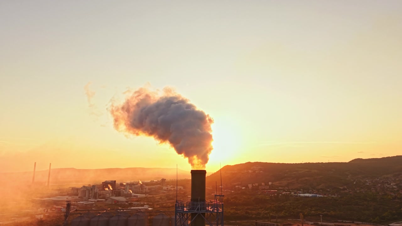 Il fumo sale da un camino di una fabbrica al tramonto in un'area industriale