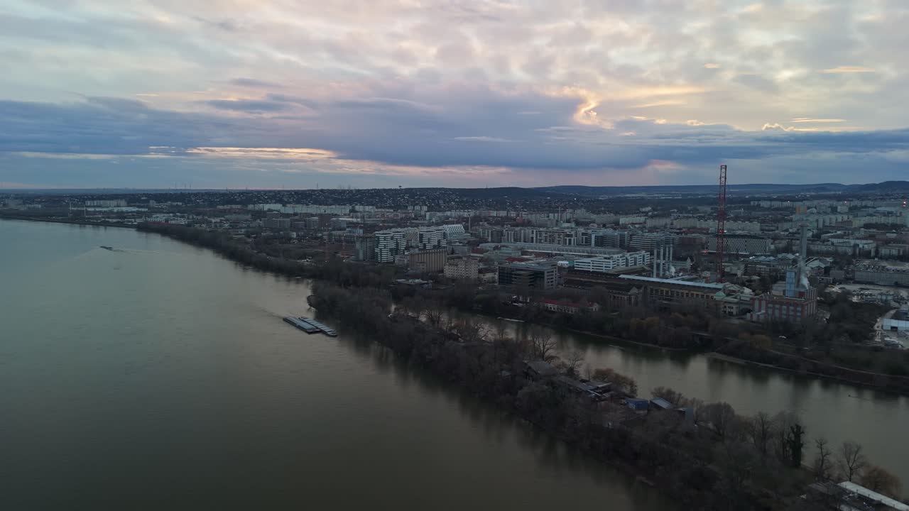 Vista aérea de drone de Budapeste, Hungria, destacando o Rio Danúbio, o horizonte urbano e a arquitetura diversa sob um céu de tarde nublado, com bairros como Kelenföld e Budafok visíveis.