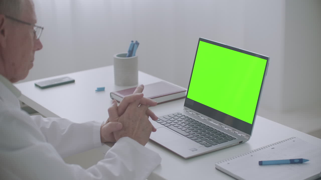médico masculino está consultando en línea mirando la pantalla verde de la computadora portátil en la oficina de la clínica tecnología clave de croma