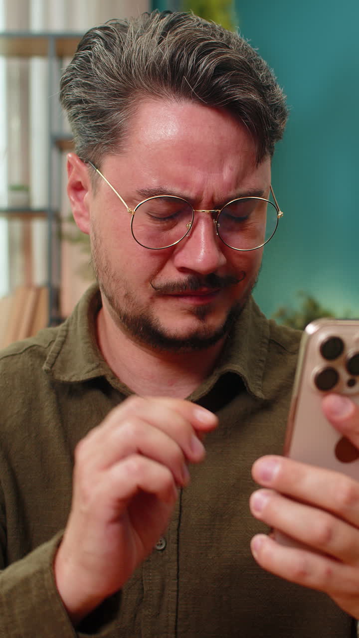 Uomo di mezza età con gli occhiali che strizza gli occhi mentre legge un testo minuscolo sullo smartphone per controllare la vista e la nitidezza