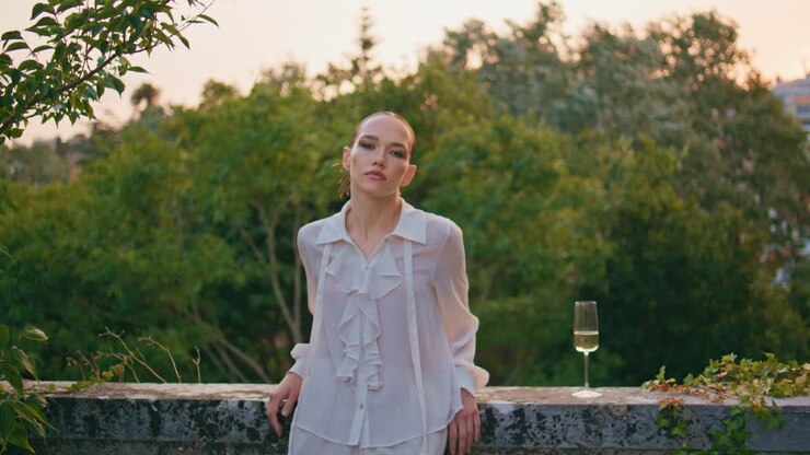 Ragazza alla moda in posa all'aperto con un bicchiere di vino che guarda la fotocamera. Donna sul balcone.