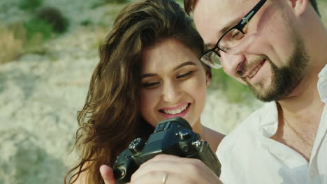 una pareja joven mira las fotos en una cámara digital sentada al lado de la playa grandes recuerdos de h