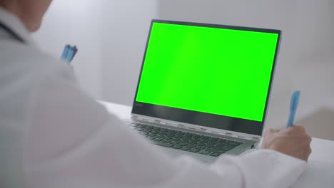 la mujer está consultando en línea, mirando la pantalla verde de la computadora portátil para la tecnología de llave cromática, escribiendo notas en el cuaderno