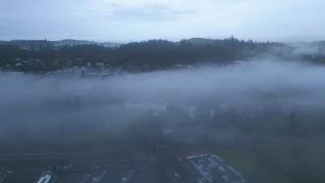 drone approaching a lakeside village shrouded heavily by mist and fog, located in the county of cumbria in united kingdom