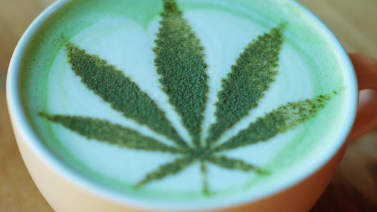Vista dall'alto di un matcha latte in una tazza di ceramica, decorato con tè verde in polvere che forma un motivo a foglia che ricorda una foglia di cannabis.