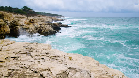 Sea-waves-breaking-on-rocky-coast-forming-foam,-panoramic-movement