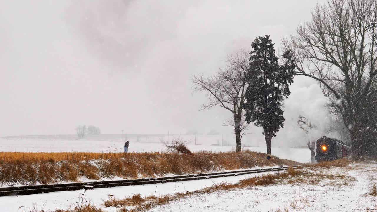 증기 기관차가 눈보라 속에서 다가올 때 철로 옆에서 개를 산책시키는 남자