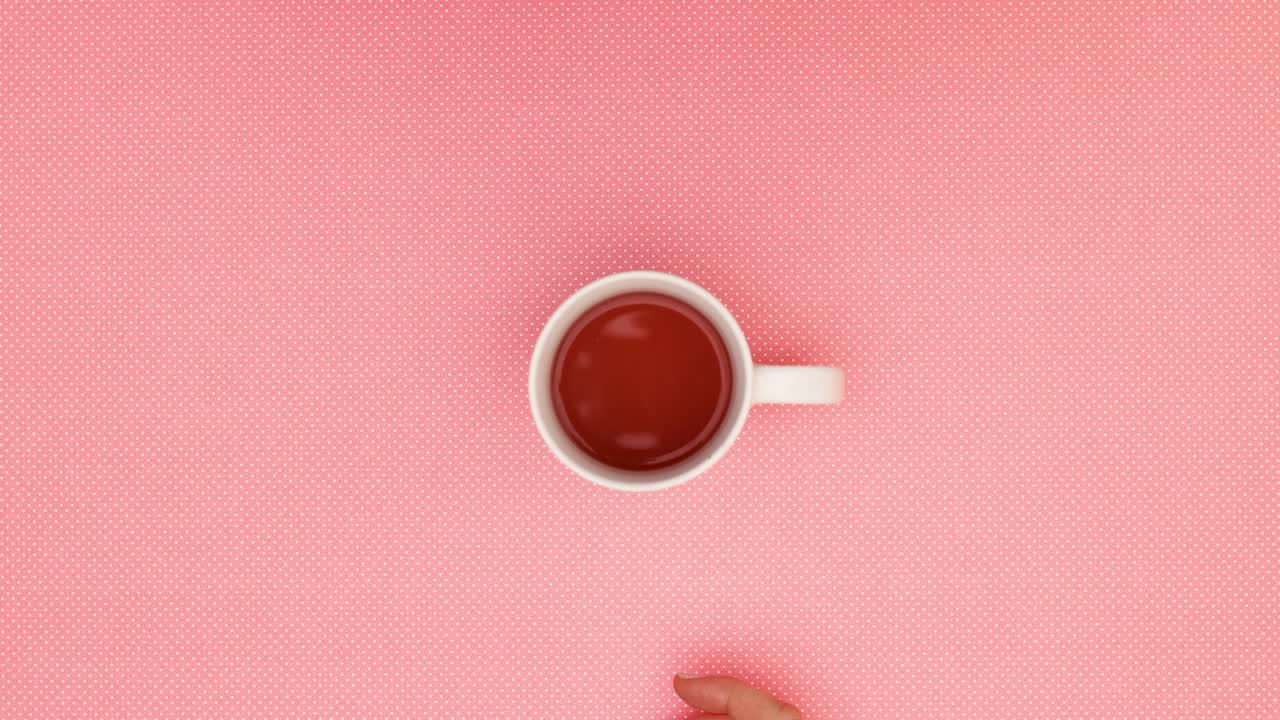 Dito di donna che sposta una tazza di porcellana di tè in cerchio su sfondo rosa - Stop motion