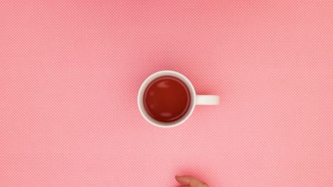 woman finger move porcelain cup of tea in circle on pink background - stop motion