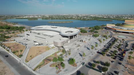aerial view of a modern architectural building complex situated by a lake with a distant cityscape.