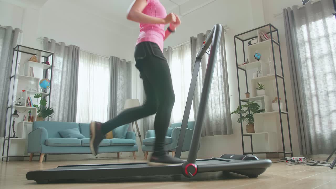 自宅でルームランナーで走るアジア人女性の横からの姿。