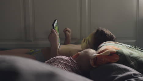 older brother on a tablet with younger baby sister