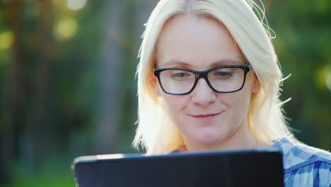 retrato de una mujer joven con gafas disfrutando de una tableta en el parque hermoso resplandor solar 4k lento