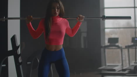 a woman performs a circular exercise on her thigh muscles. she performs squats to work out the buttocks with a barbell.