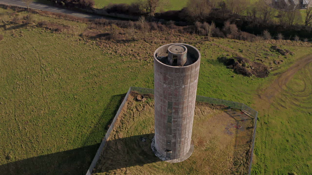 Dynamic aerial shot capturing the imposing water tower, pulling back to reveal the expansive Irish landscape surrounding it