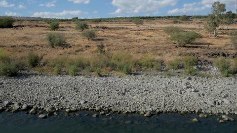 flying low over water towards the rocky shore coast line and to an arid plain with trees