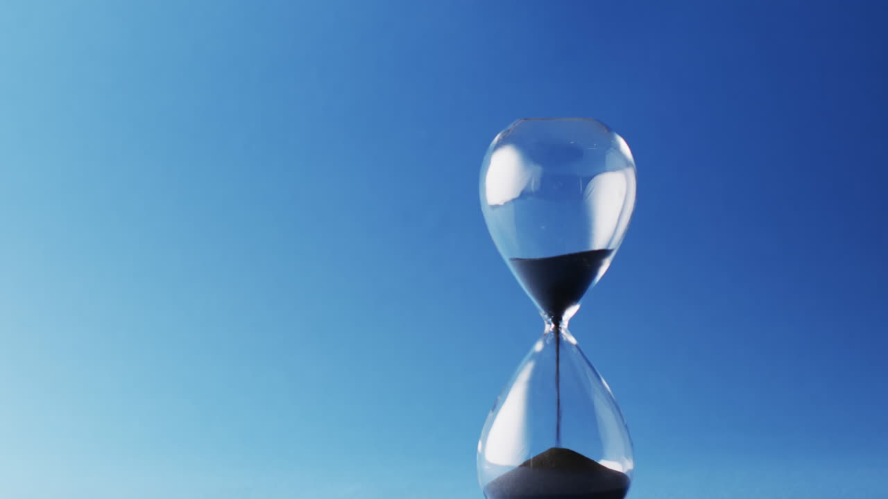 video de reloj de arena con arena negra vertiendo con espacio de copia en fondo azul