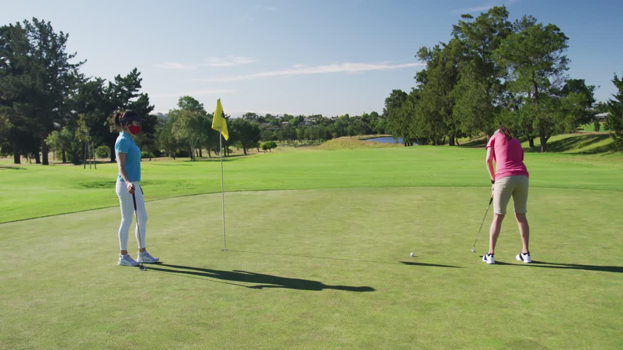 Due donne caucasiche che giocano a golf e indossano maschere, una che esegue un colpo dal bunker.