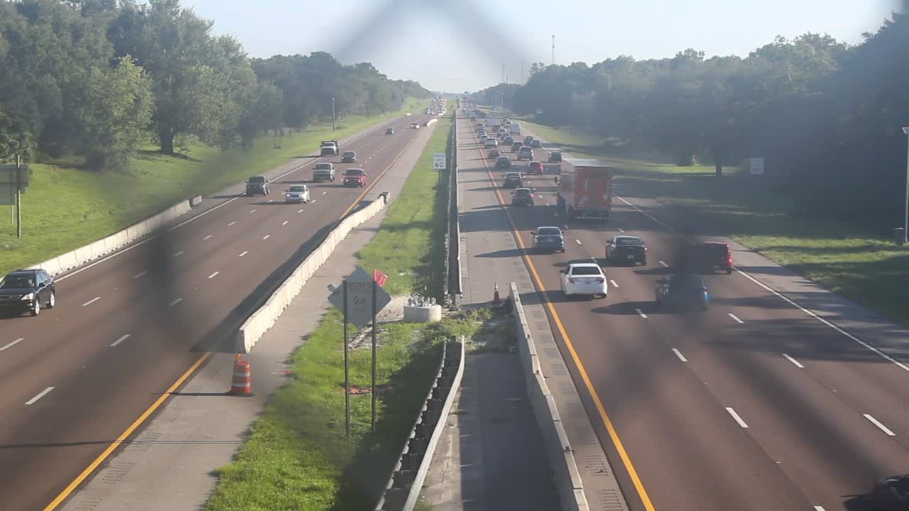 Cars speed up and down freeway, still shot, day, through fence on overpass.