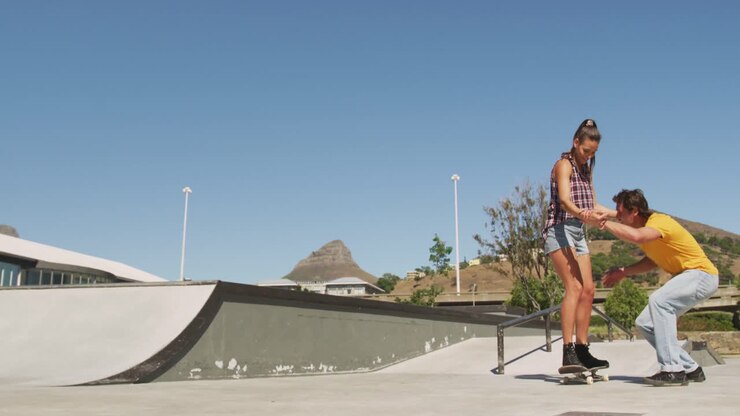 Un uomo caucasico sorridente che insegna a una donna come fare skateboard in una giornata di sole.