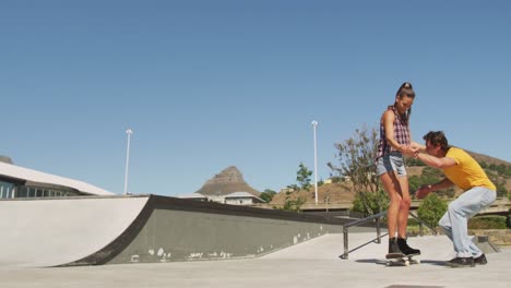 hombre caucásico sonriente enseñando a una mujer cómo patinar en un día soleado